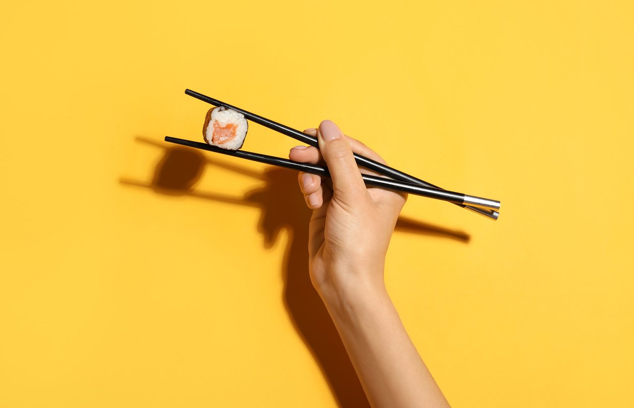 Woman Holding Chopsticks with Salmon Sushi Roll on Color Background